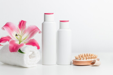 Fototapeta na wymiar Blank white bottles of shampoo, shower gel or body lotion with towel, pink lily and wooden massager. Spa concept