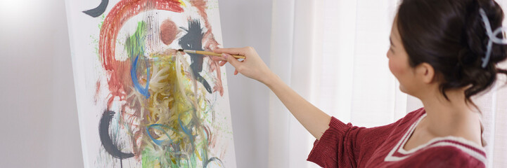 Creative of art concept, Young asian woman sit in studio and hold paintbrush to pointing on artwork
