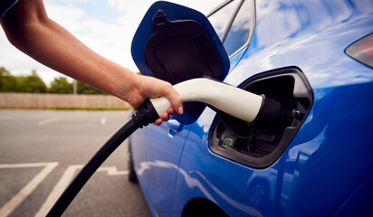 Close Up Of Hand Attaching Charging Cable To Environmentally Friendly Zero Emission Electric Car