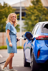 Woman Attaching Charging Cable To Environmentally Friendly Zero Emission Electric Car Outdoors