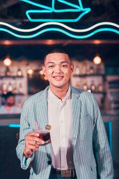 A handsome asian man looking dapper enjoying Cuba libre or Rum and Cola drink at a trendy outdoor bar or cafe.
