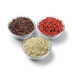 Three glass bowls with superfood, dried goji berries , cacao nibs and hemp seed isolated on white background