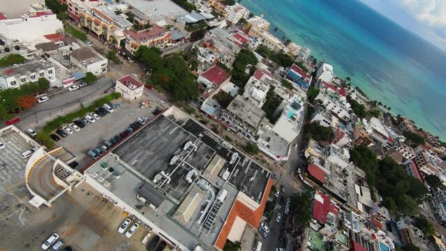 Panning drone view of the colorful buildings and rooftops in the holiday resort town of Playa del Carmen, Quintana Roo, Mexico on a bright sunny day.