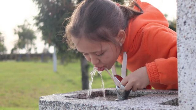 Portrait of a child girl drinks water in drinking fountain, at city park, 4k footage