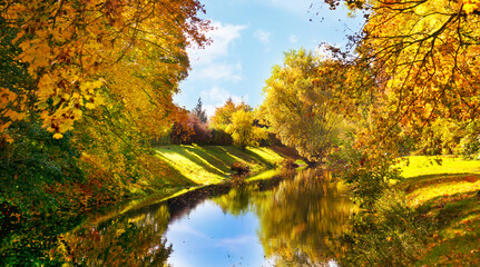 beautiful autumnal landscape with colorful trees, fall leaves and flowing water, blue sky...