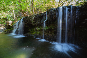 A creek with a waterfall in the middle of the woods in the pre-Alps during a spring day, near the town of Varese, Lombardy, Italy - April 2022.