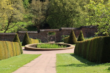 A gravel pathway leads down to a circular pond in the kitchen garden of an English stately house