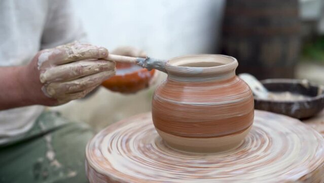 The master potter paints a clay jug with white paint on an old potter's wheel, twists his foot. Drawing a pattern on a ceramic vase.