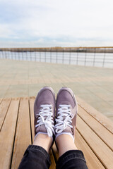 Womens legs in pink sneakers. Womens sports shoes on wooden planks on background of river. Side view. First person view