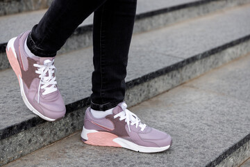 Fototapeta na wymiar cropped image of female legs in shoes. Woman in pink sneakers descend stairs