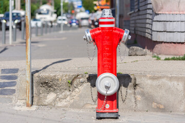Front side of a hydrant made of metallic material being on a sidewalk in a city. Blurred background