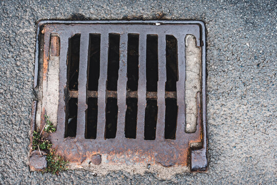 Metallic drainage cap in square shape with weeds growing at the edge of it