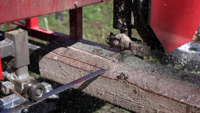 Closeup footage of an industrial reciprocating band saw chopping the bark from tree trunks. Timber slat production detail with copy space.