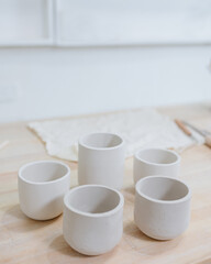 woman ceramist in the workshop makes mugs out of clay. a small business or hobby is the creation of ceramic products. an oriental young woman ceramist makes dishes and vases out of clay. handmade