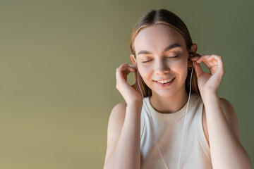 joyful woman with closed eyes listening music in wired earphones isolated on green.
