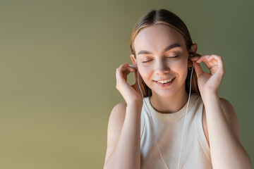 Fototapeta premium joyful woman with closed eyes listening music in wired earphones isolated on green.