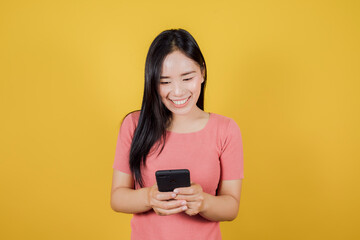 Portrait of smiling asian woman using a smartphone on yellow background