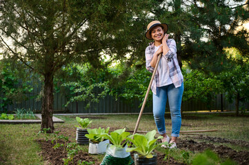 Charming African American woman, gardener smiles at the camera, posing with a hoe while working in...