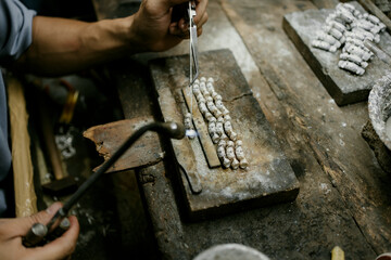 Close-up of a hand of a goldsmith who builds a precious jewel with silver. To make the jewel it...
