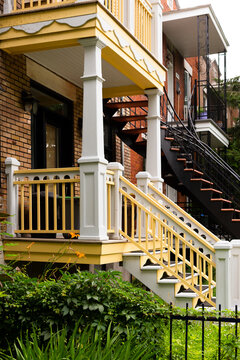 Vertical selective focus view of ornate wooden yellow and white staircases and balconies next to more common metal spiral stairs in a Rosemont borough residential street, Montreal, Quebec, Canada
