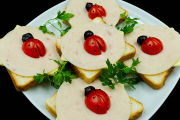 Ladybug themed sandwich plate made with tomatoes, toast bread, salami, cheddar and olives garnished with parsley