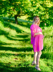 Beautiful young pregnant woman in the forest at sunset in a pink dress