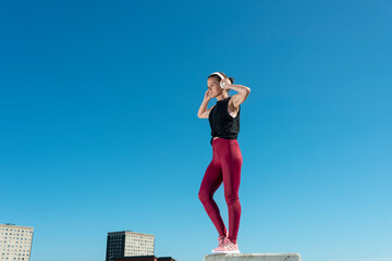 Rear view of a sporty woman holding heaphones on her head. rear view, urban background.