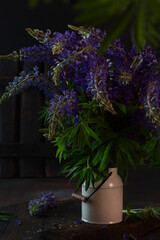 Enameled can with lupines on the table. A farmhouse.Wildflowers. Vertical photo on a dark background.
