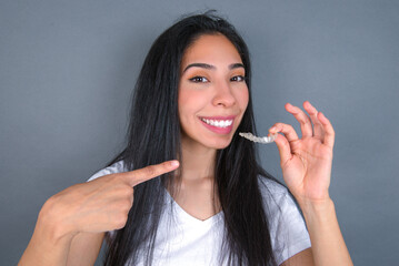 young beautiful brunette woman wearing white t-shirt over grey background holding an invisible...