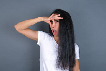 Fototapeta premium Displeased young beautiful brunette woman wearing white t-shirt over grey background plugs nose as smells something stink and unpleasant, feels aversion, hates disgusting scent.