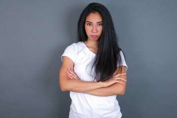Picture of angry young beautiful brunette woman wearing white t-shirt over grey background looking...