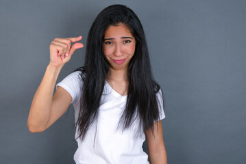 Upset young beautiful brunette woman wearing white t-shirt over grey background shapes little...