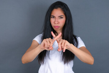 young beautiful brunette woman wearing white t-shirt over grey background has rejection angry...