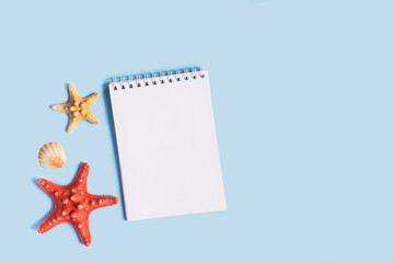 Fototapeta na wymiar To do list or blank notebook with set of starfish, sea shell on blue background. Travel, summer vacation or weekend, packing plan. lat lay, top view, copy space, place for text, minimal composition