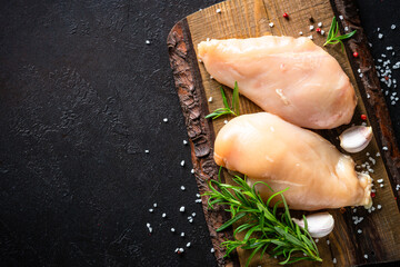 Chicken fillet breast with spices and herbs at craft wooden board at black slate table. Top view with space for text.