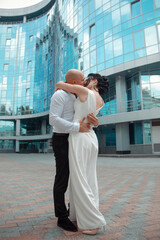 young groom and bride are standing close in hugs with love and kissing sexy on the blue glass street building background at city. romantic wedding couple. wedding concept, free space