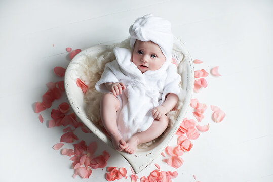 Attractive Ukrainian newborn girl in a white bathrobe and with a towel on her head, looking at the camera while sitting in the bathroom.Portrait of a beautiful,  newborn girl Closeup photo