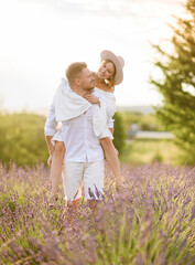 Portrait of a beautiful young couple in light summer clothes hugging in a lavender field at sunset