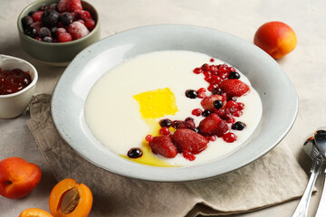 Traditional breakfast semolina porridge - creamy pudding with butter, frozen berries and fresh apricots in a grey plate