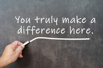 Male hand writes in white chalk pencil the word you truly make a difference here