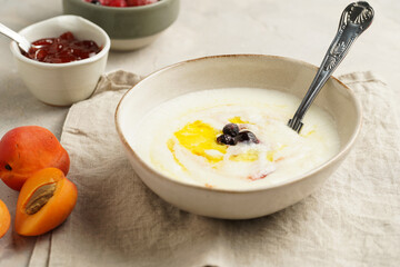 Traditional breakfast semolina porridge - creamy pudding with butter, frozen blueberries and fresh apricots in an oval plate on checkered kitchen towel