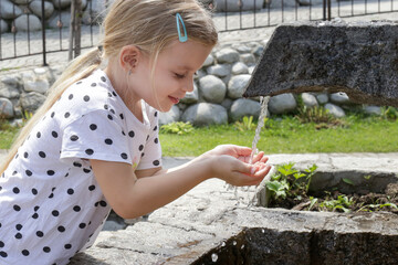 Little girl drinking clean spring water from the outdoor tap
