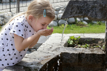 Fototapeta premium Little girl drinking clean spring water from the outdoor tap 