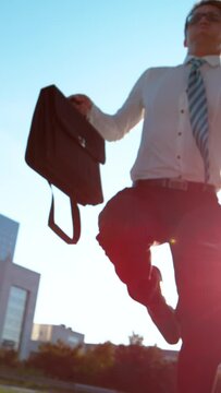 SLOW MOTION, LENS FLARE, BOTTOM UP: Young businessman in a hurry jumps over the camera as he runs to his office building. Excited Caucasian man rushing to get to an important business meeting on time.