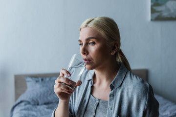 pensive woman with menopause drinking fresh water from glass.