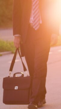 SLOW MOTION, LENS FLARE, LOW ANGLE: Sad young businessman carrying his briefcase after a bad day at work. Unrecognizable young man in a suit losing hope after another failed job interview in the city.