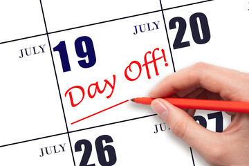 Hand writing text DAY OFF and drawing a line on calendar date 19 July. Vacation planning concept.