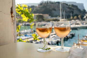 Cold rose wine in glasses served on outdoor terrace in sunlights with view on old fisherman's harbour with colourful boats in Cassis, Provence, France