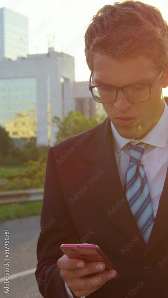 Wall mural SUPER SLOW MOTION, SUN FLARE, CLOSE UP: Young businessman anxiously browsing the internet on his smart phone as he walks down the empty sidewalk on a sunny summer evening. Yuppie receives bad news.