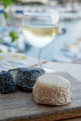 Pairing of French goat cheese crottin and glass of white French wine served with view on boats in harbor of Cassis, Provence, France